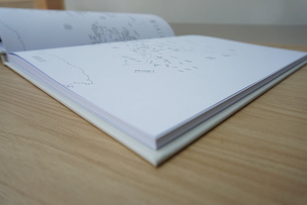 An open stone notebook or journal lying on a light wood tabletop, with faint line drawings of a map and small text visible on the pages.