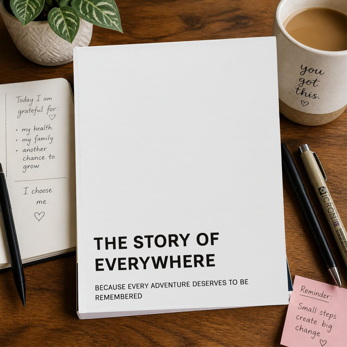 A white hardcover journal titled 'THE STORY OF EVERYWHERE' with black text, styled on a wooden desk with a coffee mug, pens, sticky notes, and a notebook.
